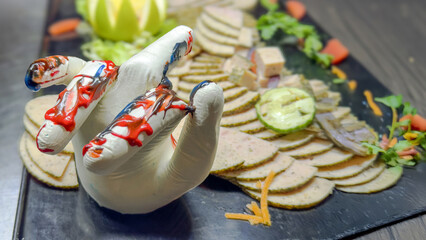 Creative food presentation featuring a hand-shaped sculpture made of white material, adorned with colorful sauces, surrounded by an array of sliced meats and garnishes, showcasing culinary artistry