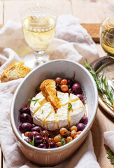 Baked Camembert cheese with grapes, thyme, and rosemary, served with white wine and a baguette.