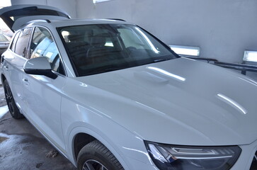 Modern white SUV with open trunk receiving professional detailing service in auto body shop,...