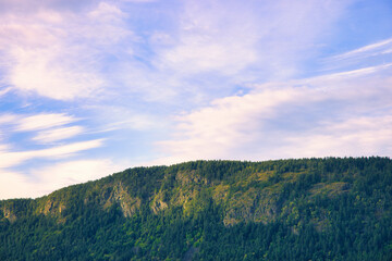 Sunset sun warmly embracing the top of a mountain, under a partly cloudy blue sky