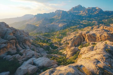 Golden hour illuminates a majestic, rugged mountain landscape. Rocky peaks frame a verdant valley, showcasing nature's vast beauty and grandeur.