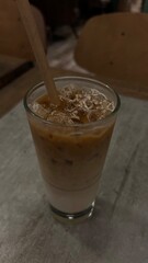 An iced latte on table with white wall background. Iced coffee in takeaway glass. Ice coffee in a tall glass with cream poured over and beans. Cold summer drink on a table. Tasty ice coffee with milk