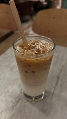 An iced latte on table with white wall background. Iced coffee in takeaway glass. Ice coffee in a tall glass with cream poured over and beans. Cold summer drink on a table. Tasty ice coffee with milk