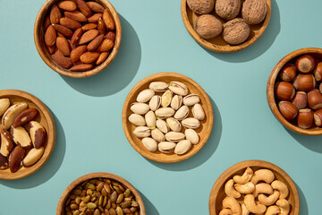 Assorted nuts and seeds in wooden bowls arranged on a pastel background