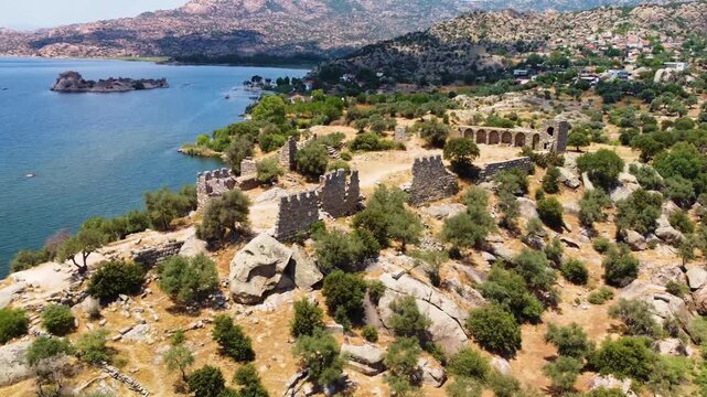 aerial perspective showcasing the serene blue waters of Lake Bafa, nestled against a rugged landscape dotted with ancient ruins and lush Mediterranean vegetation in Turkey.