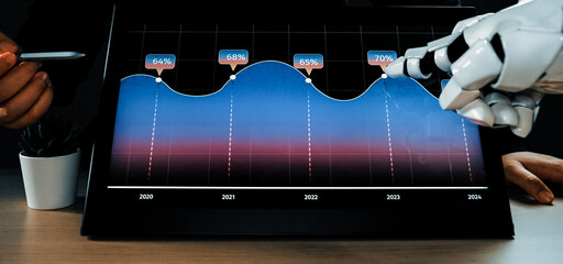 A robotic hand interacts with a digital screen displaying data trends. The image captures the essence of modern technology and its application in business analysis.Noogenesis