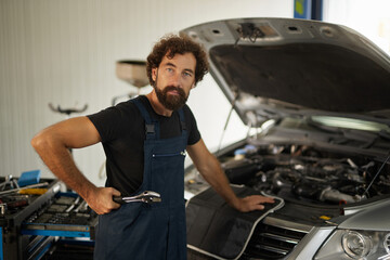 A skilled car mechanic is working under the hood of a vehicle in an automotive repair shop. The mechanic uses tools to ensure the car is operating efficiently.