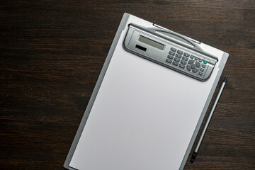Clipboard with a white blank paper and pencil on wooden table, closeup, top view. Grey desktop with...