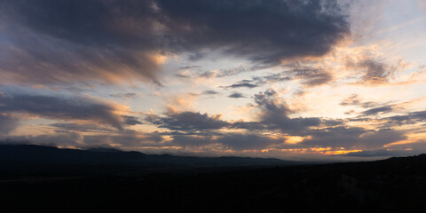 Dramatic cloudy sunset over dark silhouetted mountains with vibrant orange and purple hues in the sky