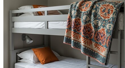 A grey bunk bed with white linens, orange and patterned pillows, a patterned blanket, and a wall-mounted lamp.