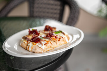 Flatbread with melted cheese and caramelized onions served on a white plate outdoors. Rustic presentation, suitable for menu design, food photography, or culinary content.