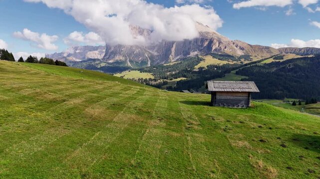 Aerial view over meadows in front of Alpe di Siusi peaks, in Dolomites, Italy. Beautiful hut on alpine plateau Seiser Alm. Wooden cabins in south Tyrol. Dolomites UNESCO World Heritage.