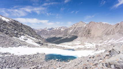 Aerial view of a rocky mountain landscape with a small lake and patches of snow under a blue sky