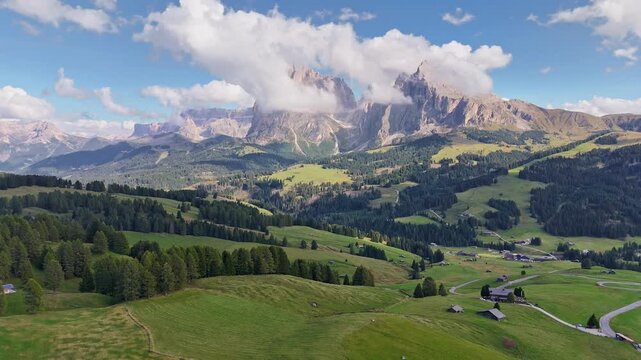 Aerial view over meadows in front of Alpe di Siusi peaks, in Dolomites, Italy. Beautiful hut on alpine plateau Seiser Alm. Wooden cabins in south Tyrol. Dolomites UNESCO World Heritage.