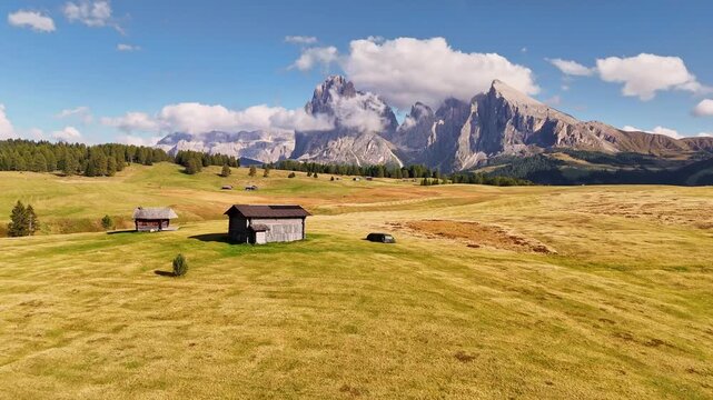 Aerial view over meadows in front of Alpe di Siusi peaks, in Dolomites, Italy. Beautiful hut on alpine plateau Seiser Alm. Wooden cabins in south Tyrol. Dolomites UNESCO World Heritage.