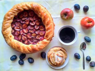 homemade plum pie, apple bun with cinnamon and a cup of coffee on the table, top view