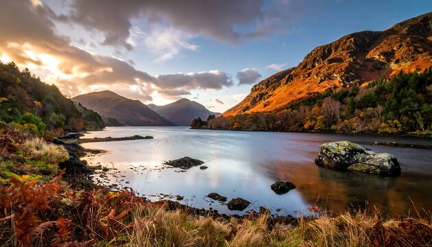 A scenic landscape of a tranquil lake surrounded by mountains and autumn foliage under a dramatic, cloudy sky during sunset