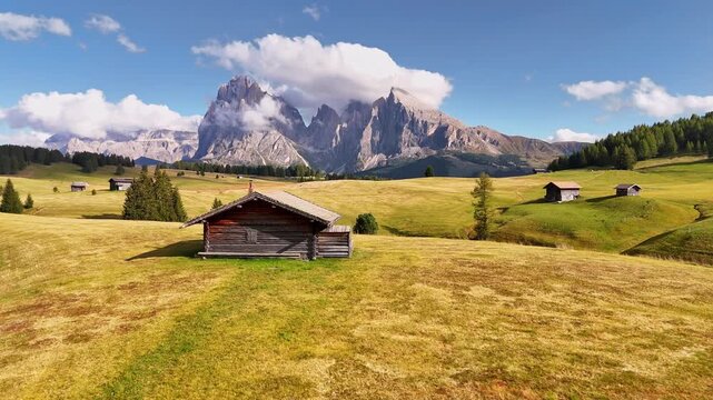 Aerial view over meadows in front of Alpe di Siusi peaks, in Dolomites, Italy. Beautiful hut on alpine plateau Seiser Alm. Wooden cabins in south Tyrol. Dolomites UNESCO World Heritage.