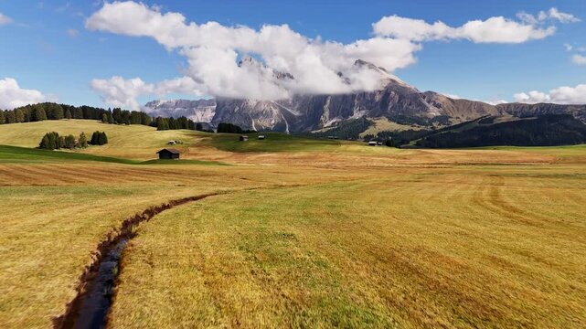 Aerial view over meadows in front of Alpe di Siusi peaks, in Dolomites, Italy. Beautiful hut on alpine plateau Seiser Alm. Wooden cabins in south Tyrol. Dolomites UNESCO World Heritage.