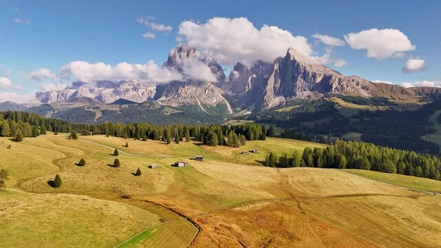 Aerial view over meadows in front of Alpe di Siusi peaks, in Dolomites, Italy. Beautiful hut on alpine plateau Seiser Alm. Wooden cabins in south Tyrol. Dolomites UNESCO World Heritage.