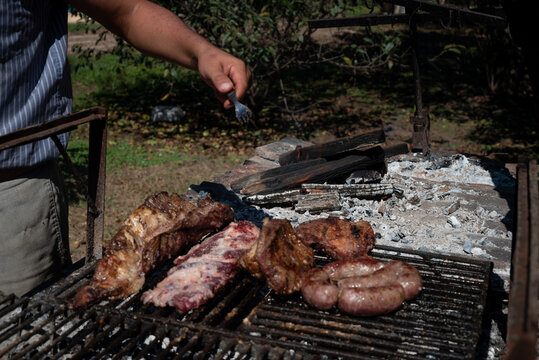 Parrilla con carne asandose, mano de asador con tenedor 
