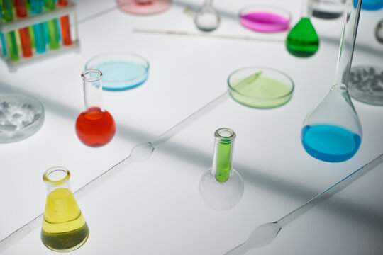 Laboratory glassware being used for conducted experiment: flasks with colorful solutions, Petri dishes with chemical substances and glass rods utilizes for mixing elements