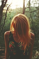 A woman with long red hair is standing in a forest. She is wearing a floral tank top and has her hair pulled back. The image has a peaceful and serene mood, as the woman is surrounded by nature
