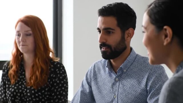 Three people in a meeting room with one woman in a black polkadot shirt