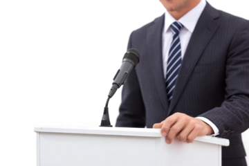 A man in a dark suit and striped tie stands behind a white podium with a microphone, ready to speak.