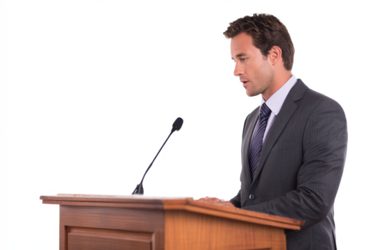 A man in a suit stands behind a wooden podium, delivering a speech with a microphone.