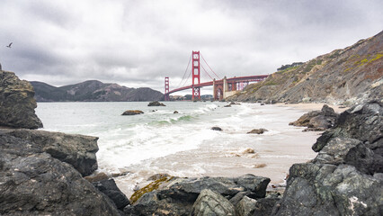 Golden gate bridge view from a rocky beach with waves and cloudy sky in san francisco california usa
