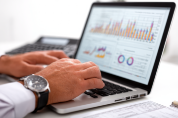 Close-up of a person's hands typing on a laptop displaying business charts and data analysis.