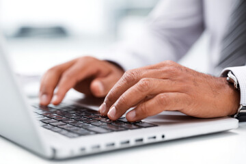 Close-up shot of a person's hands typing on a laptop keyboard in an office setting.