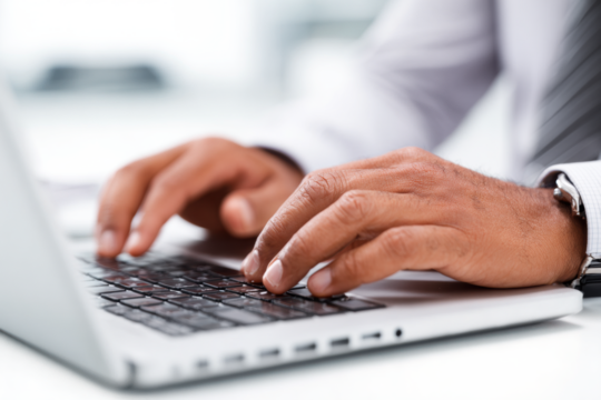 Close-up shot of a person's hands typing on a laptop keyboard in an office setting.