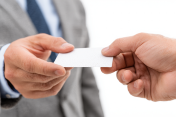 A businessman in a grey suit hands a blank white business card to another person's hand during a professional meeting.