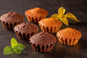Delicious assortment of muffins garnished with fresh mint leaves on dark background