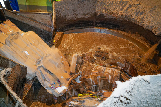 Cardboard boxes are broken down and pulped with water in a large, circular tank. This is part of the paper recycling process at a recycling plant or factory