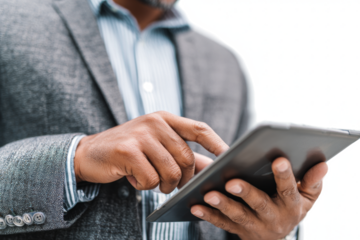 A businessman in a grey blazer and striped shirt uses his finger to navigate a black tablet against a white background.