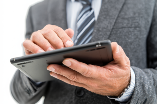 Close-up of a businessman in a formal suit and tie using a black digital tablet, interacting with the touchscreen.