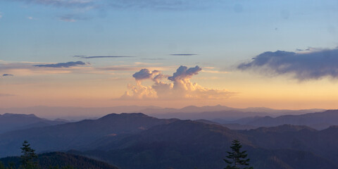 Scenic view of distant mountains with layered ridges under a pastel colored sky and fluffy clouds