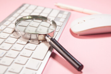 Magnifying glass and computer keyboard on pink background. Business concept.