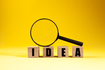 Idea word on wooden cubes with magnifying glass on yellow background