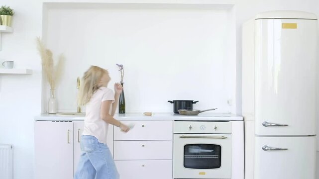 Happy 9 years old girl dancing and singing in kitchen at home using rolling pin as microphone
