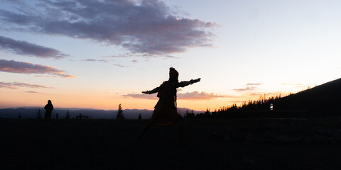 Silhouette of person with arms outstretched against a colorful sunset sky and distant mountain range © Rodrigo