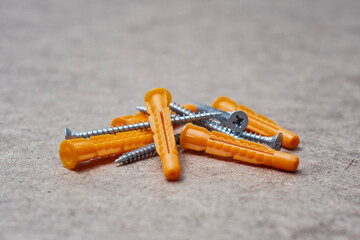 Set of orange plastic dowels and silver metal screws laying on wooden surface. Essential hardware fasteners for mounting and installing.