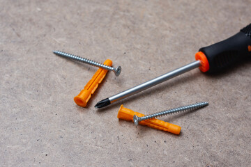 Close up of a manual screwdriver with metal screws and orange wall plugs on a wooden surface. Concept of DIY tools, construction equipment for home repair and installation.