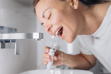 A young woman uses a portable water flosser for oral care in the bathroom. Personal hygiene and modern dental care routine. 