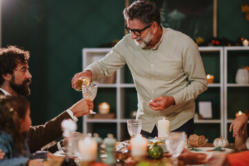 Senior man pouring wine for family celebrating thanksgiving dinner at home