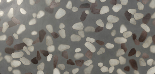 Closeup of a smooth gray surface with embedded white, gray, and brown pebbles, creating a textured and patterned background for various design applications