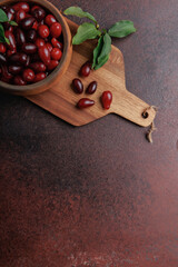 Close-up vertical shot of cornelian cherries with green leaves in wooden bowl on rustic surface